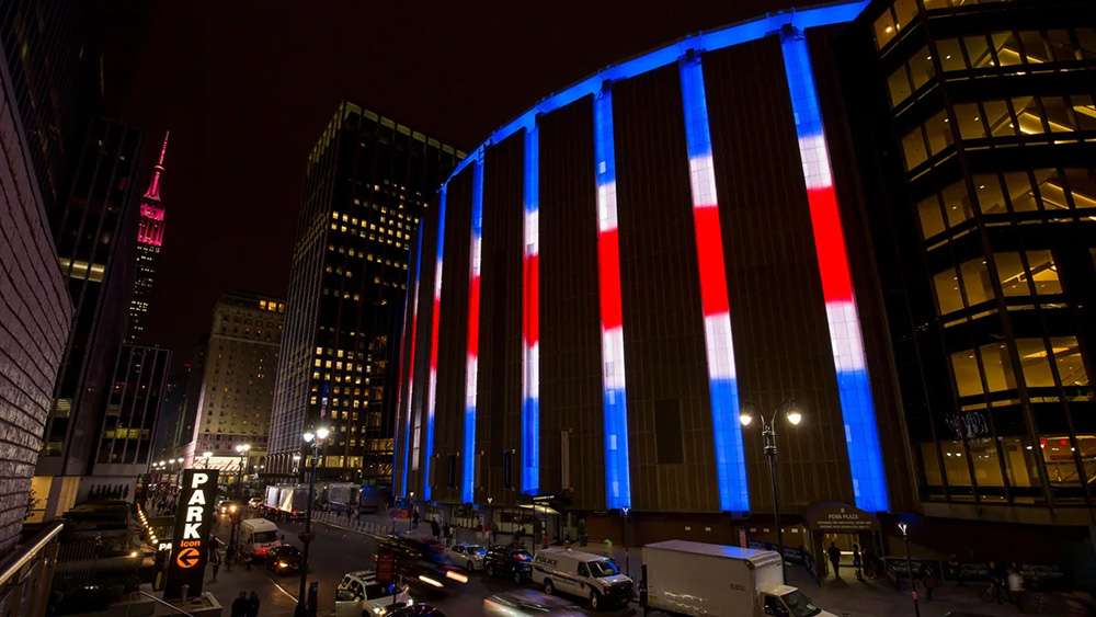 The exterior of Madison Square Garden, New York City, lit up with red, white, and blue lights.